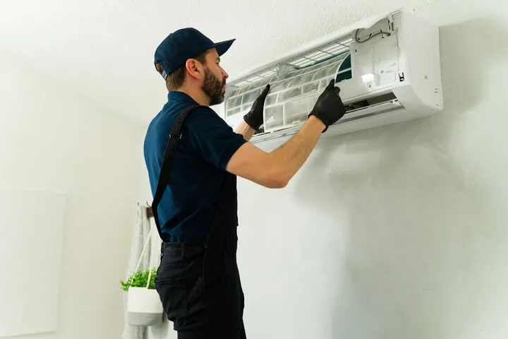 Technician in blue uniform repairing wall-mounted air conditioning unit