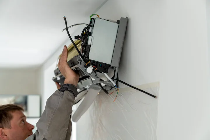 Technician installing electrical equipment on white wall with wires