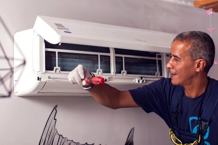 Technician repairing air conditioning unit with red tool