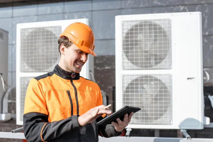 Technician in orange safety gear checks tablet near industrial air conditioning units