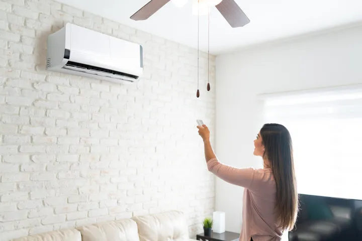 Woman adjusting air conditioning unit on white brick wall