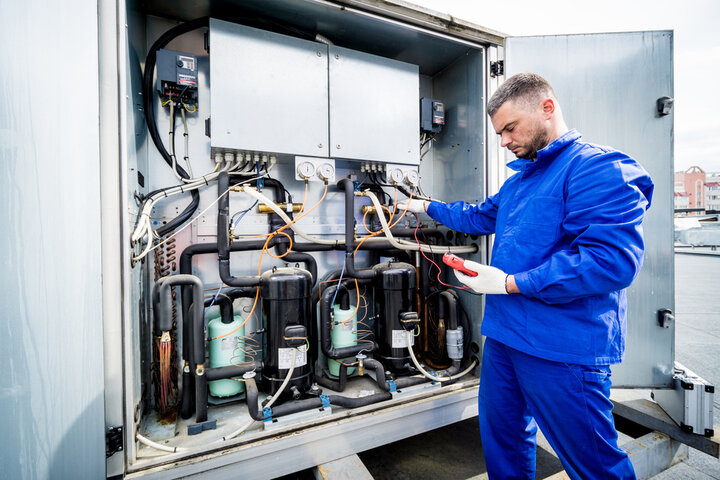 Technician in blue uniform checking industrial cooling system compressors
