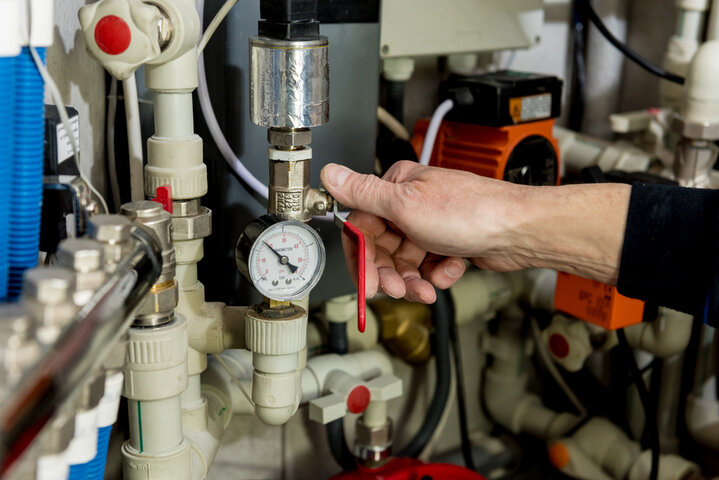 Technician adjusting pressure gauge on complex industrial piping system