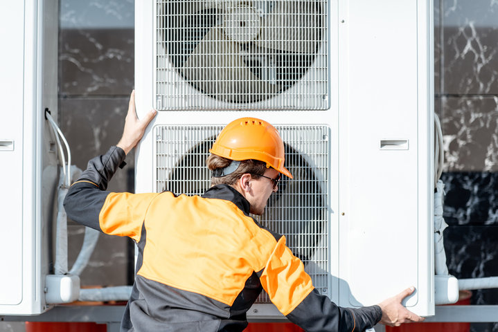 Technician in safety gear inspecting large industrial air conditioning unit