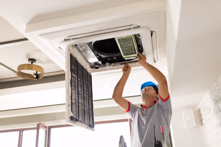 Technician installing or repairing ceiling-mounted air conditioning unit