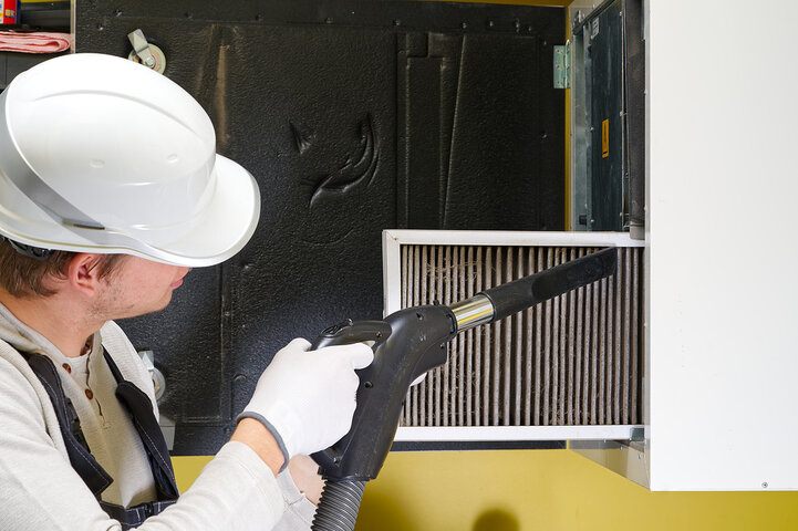 Worker in hard hat uses industrial vacuum to clean air filter