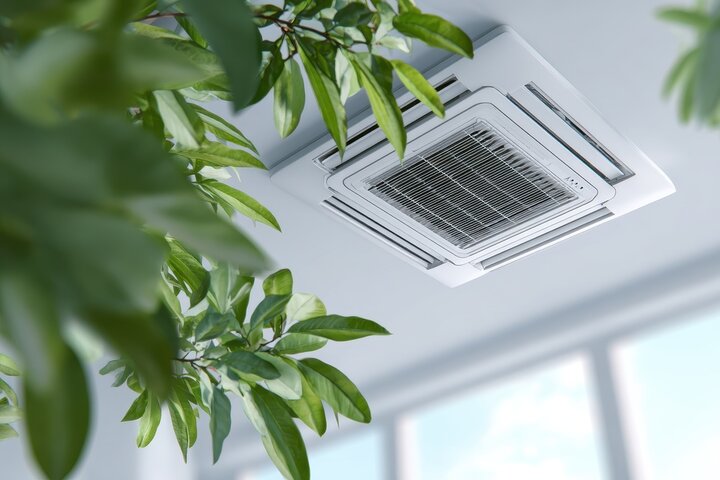 Ceiling air conditioning unit surrounded by green plant leaves