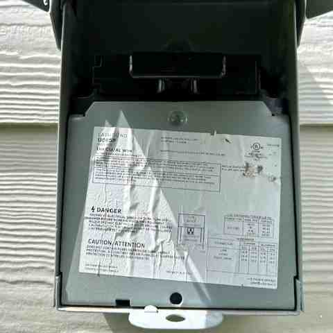 Homeowner safely turning off the electrical disconnect switch on an outdoor AC unit - how to clean your ac condenser unit