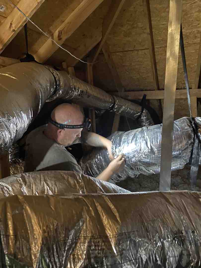 Technician inspecting home attic insulation and ductwork for energy efficiency