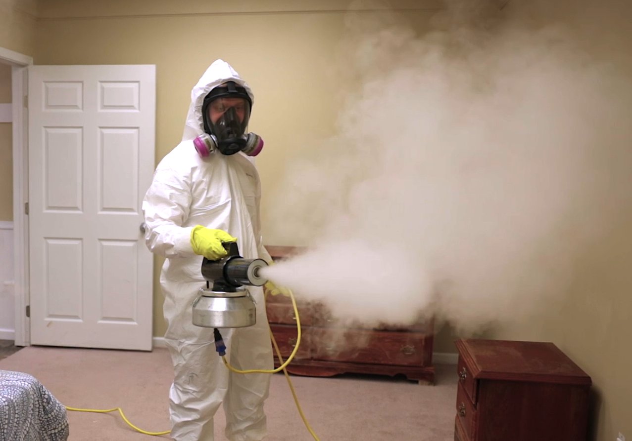 Restoration technician in full PPE fogging an interior space during a remediation job.