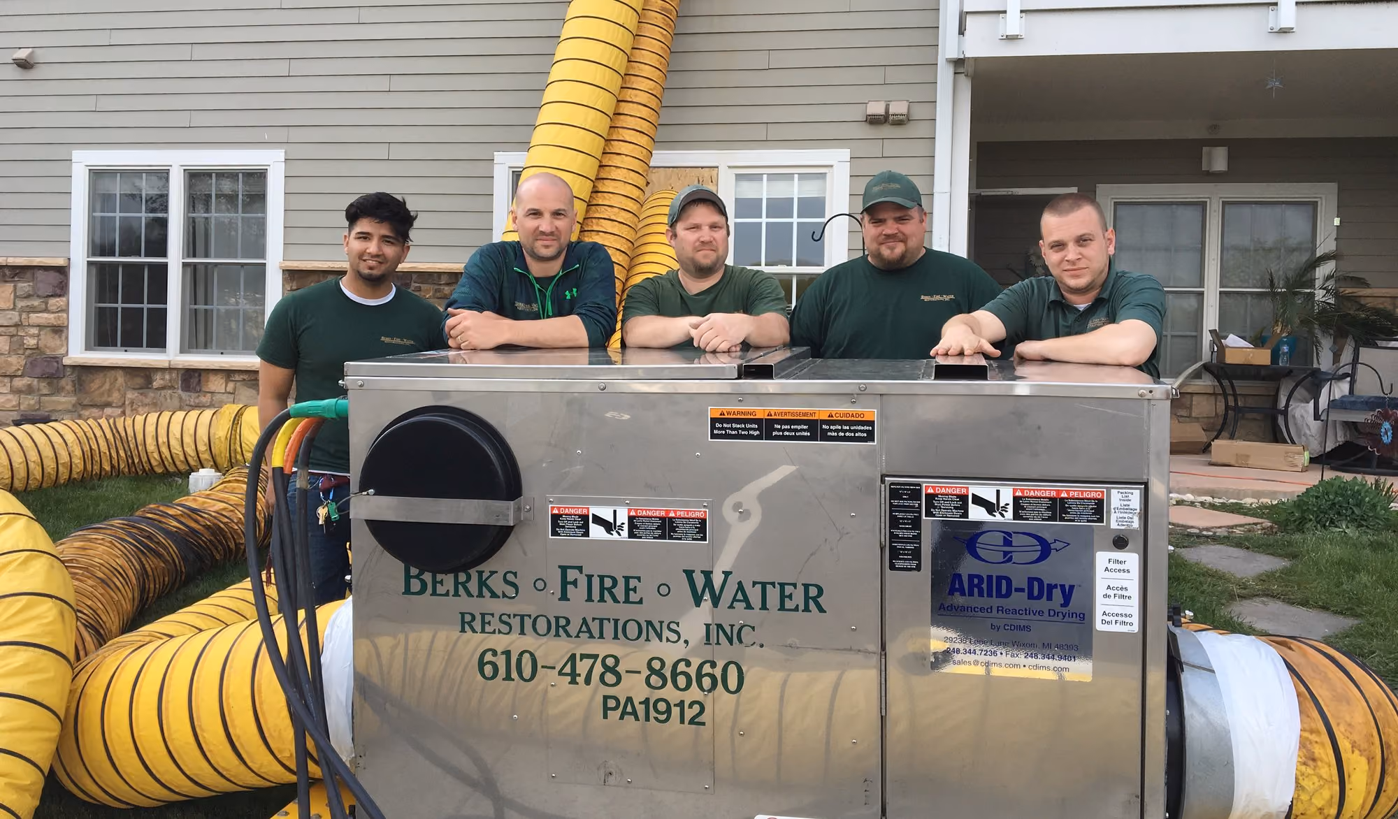 Five Berks Fire Water crew members with a trailer-mounted ARID-Dry drying unit and ducting outside a customer's home