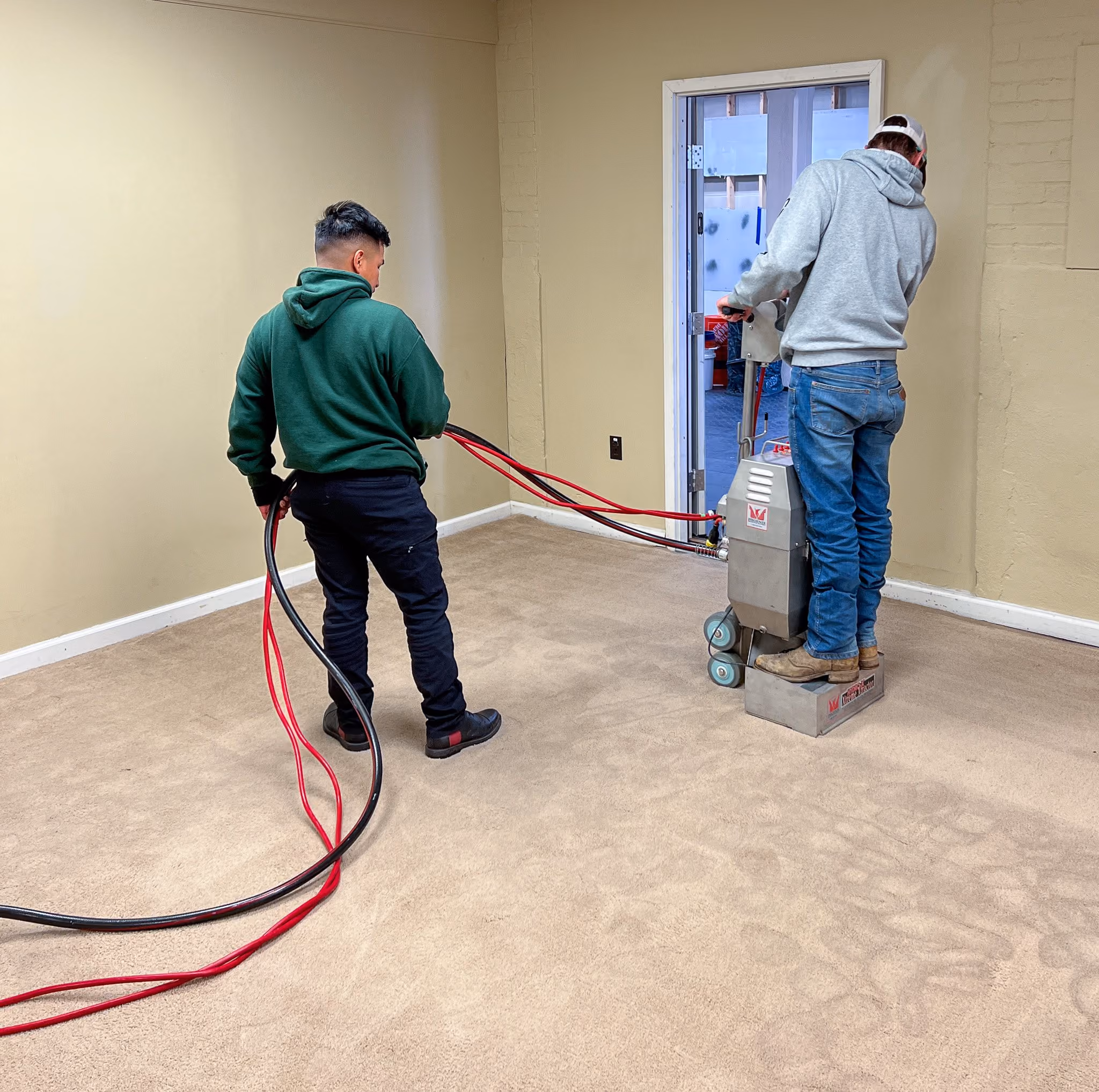 Two technicians operating a weighted extraction tool on carpet in the training space