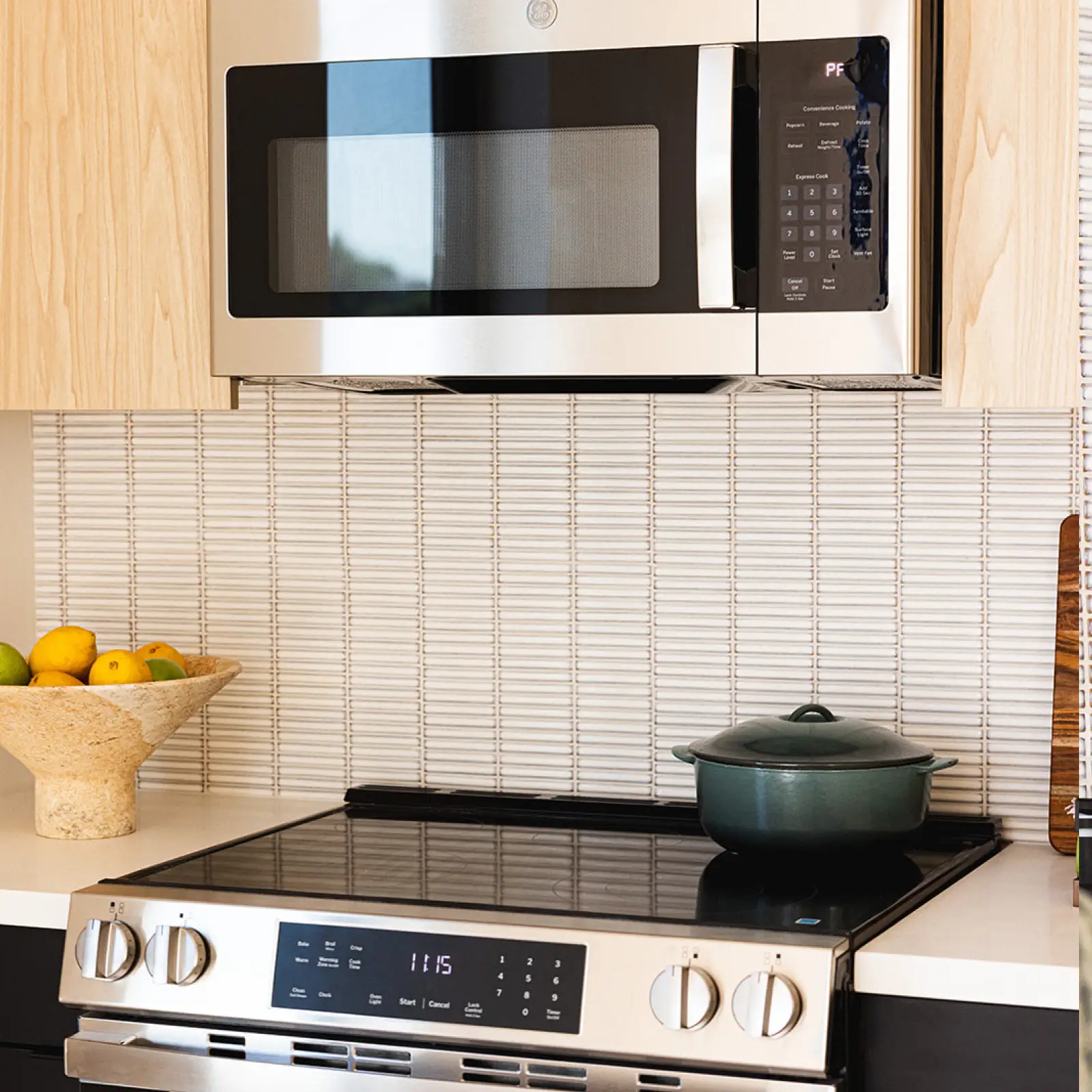 Modern kitchen with stainless steel microwave and stove, a green pot on the stovetop, and a bowl of lemons and limes on the counter.