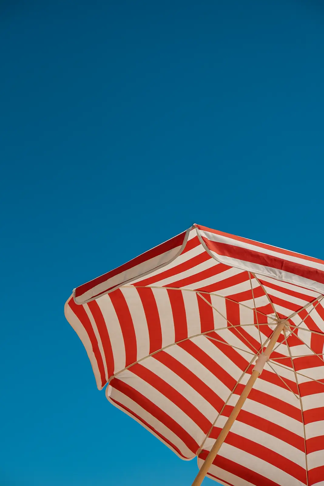 Red and white striped beach umbrella against a clear blue sky.