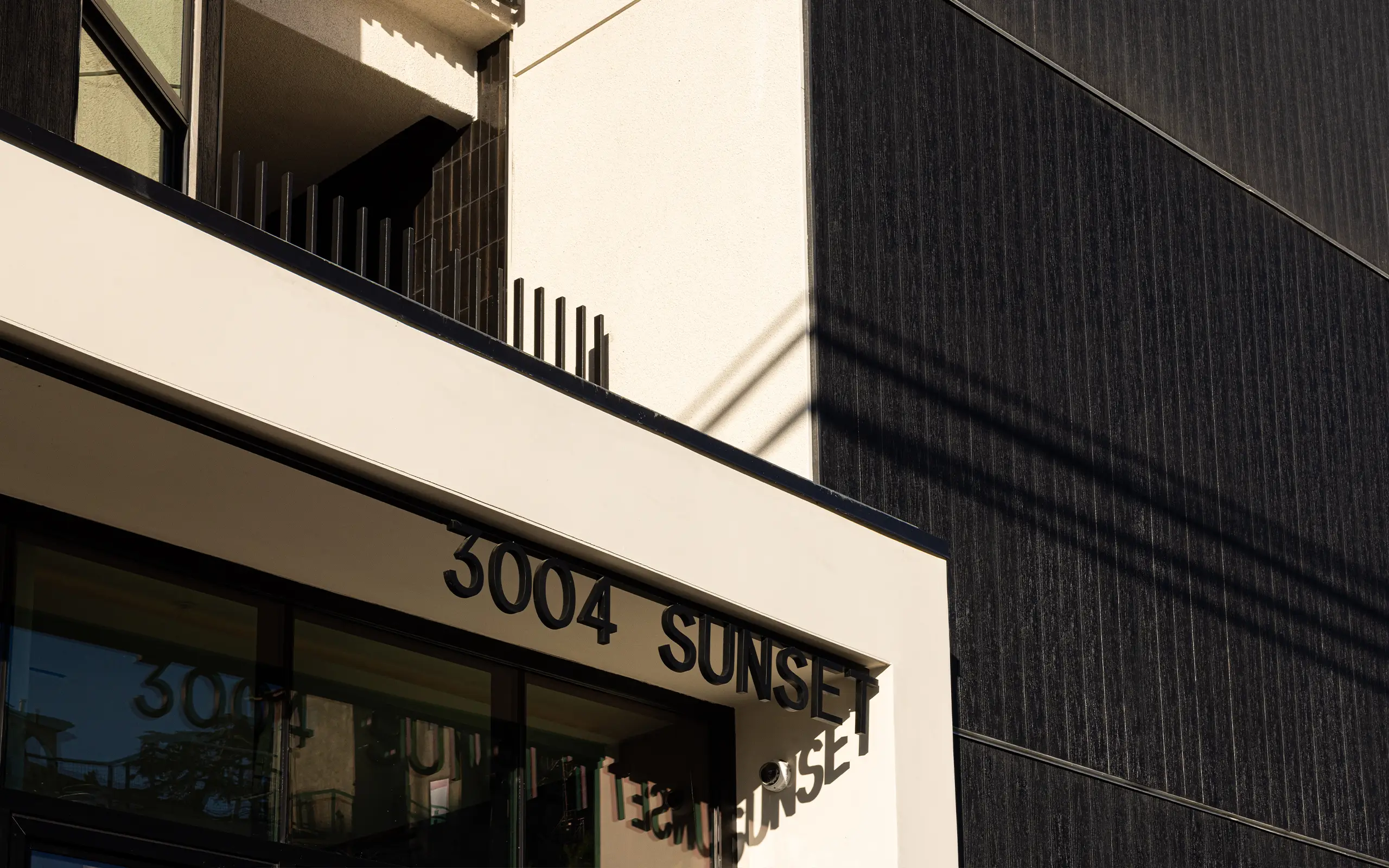 Modern Mysa Apartments building entrance with address number '3004 SUNSET' casting shadow on white wall.