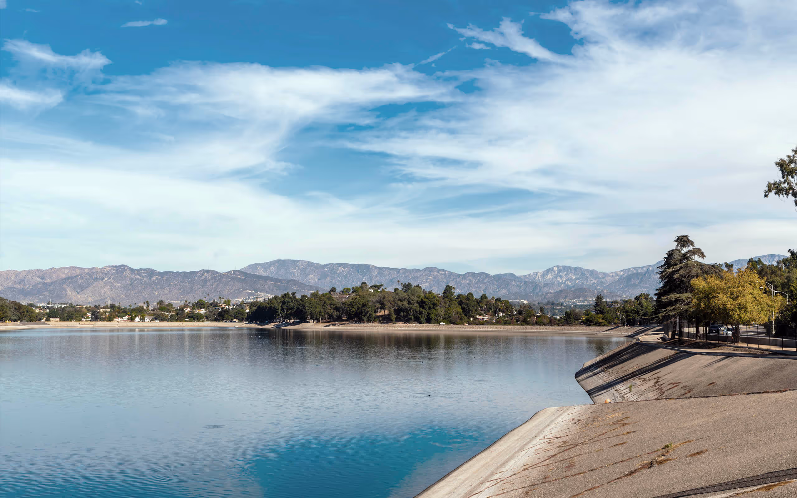 Still water surface and and pathways around reservoir with mountain range in the bakground