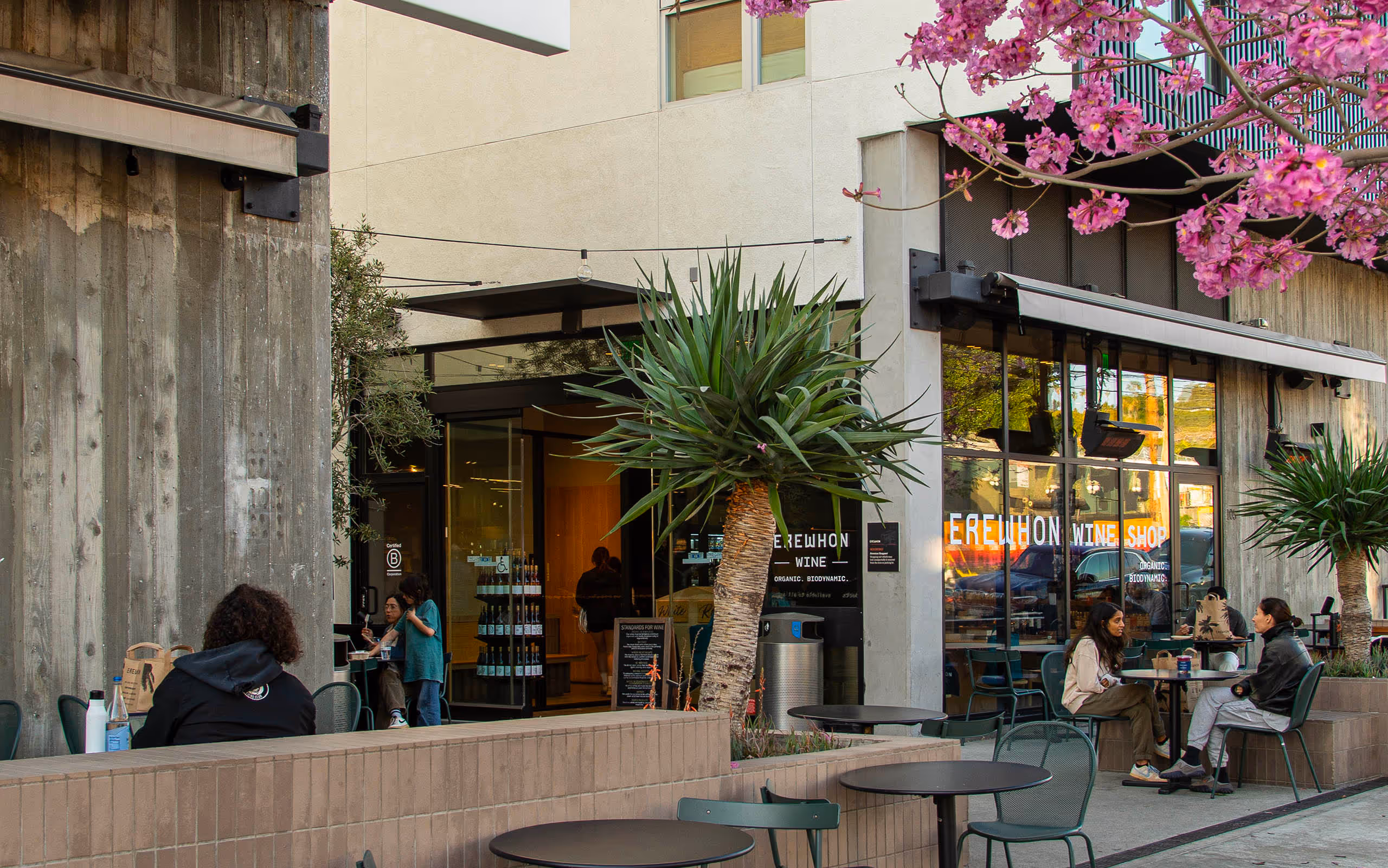 Sidewalk with tables and people outside of Erewhon wine shop