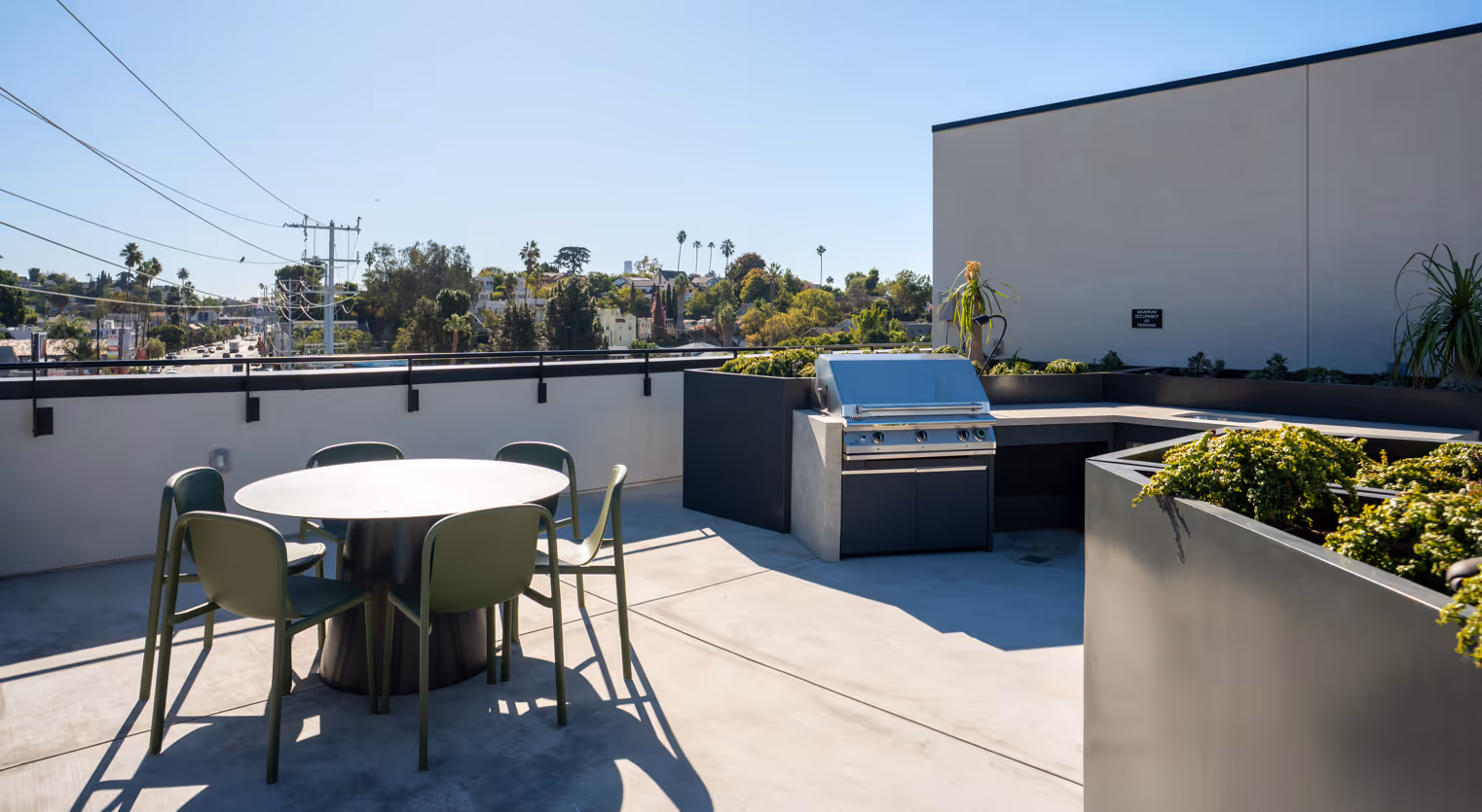 Sunny rooftop terrace with outdoor seating including green chairs around black tables and wicker armchairs with dark cushions.