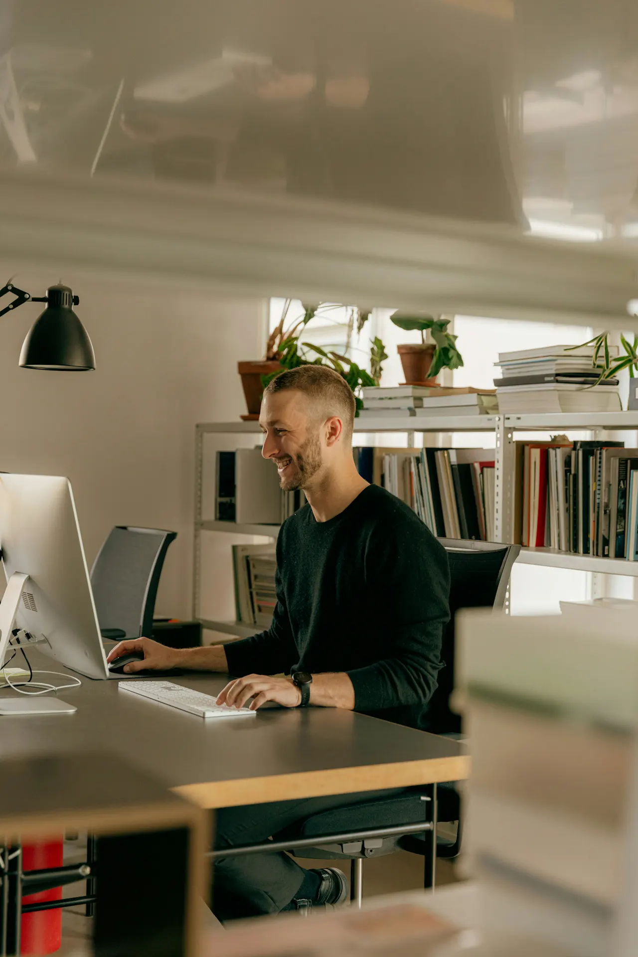 Leende man vid skrivbord framför dator i ljust kontor
