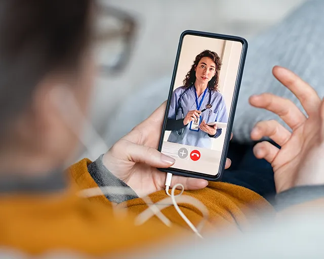 Person håller en smartphone och har videosamtal med en kvinnlig läkare i sjukvårdskläder.