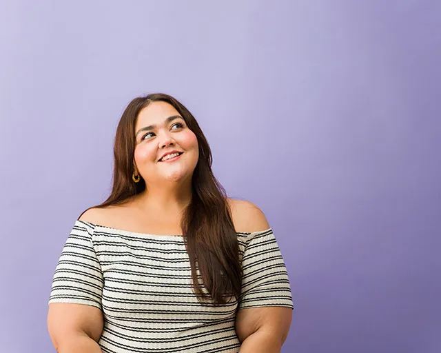Leende kvinna med lång brunt hår och off-shoulder randig tröja mot lila bakgrund.