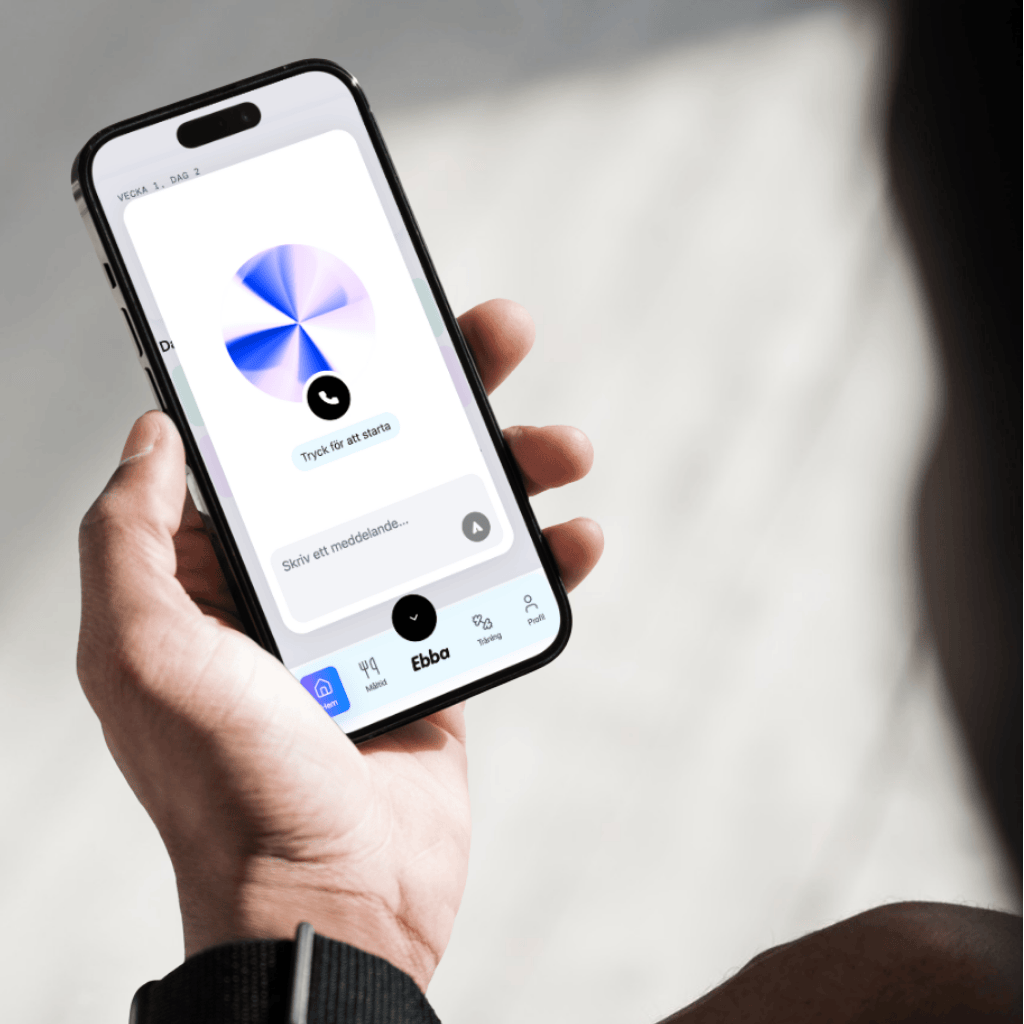 En hand håller en smartphone som visar en app som heter Ebba med funktioner som matked, tracking och profil, samt en knapp med texten 'Tryck för att starta'.