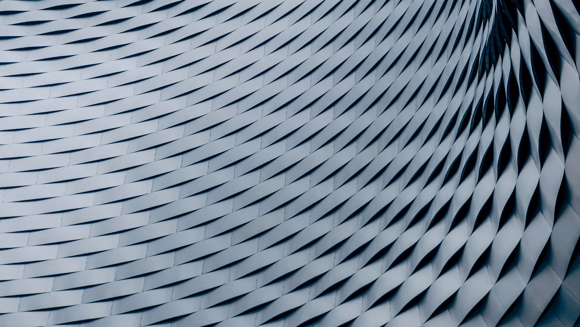 Surface de bâtiment avec motif géométrique en treillis ondulé métallique gris.
