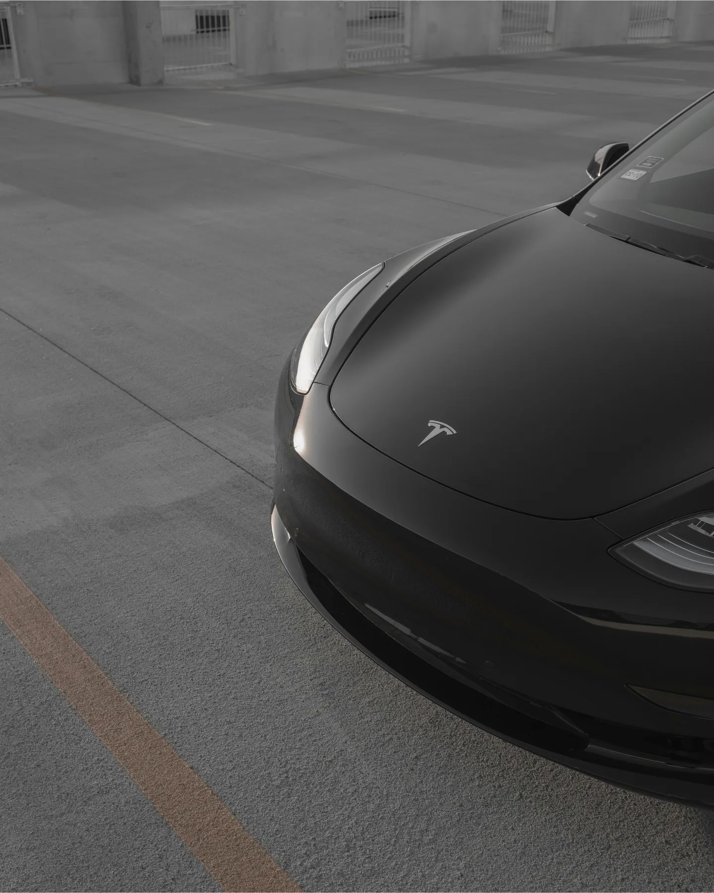A close-up view of a sleek black Tesla parked on a concrete surface, showcasing its modern design and emblem.