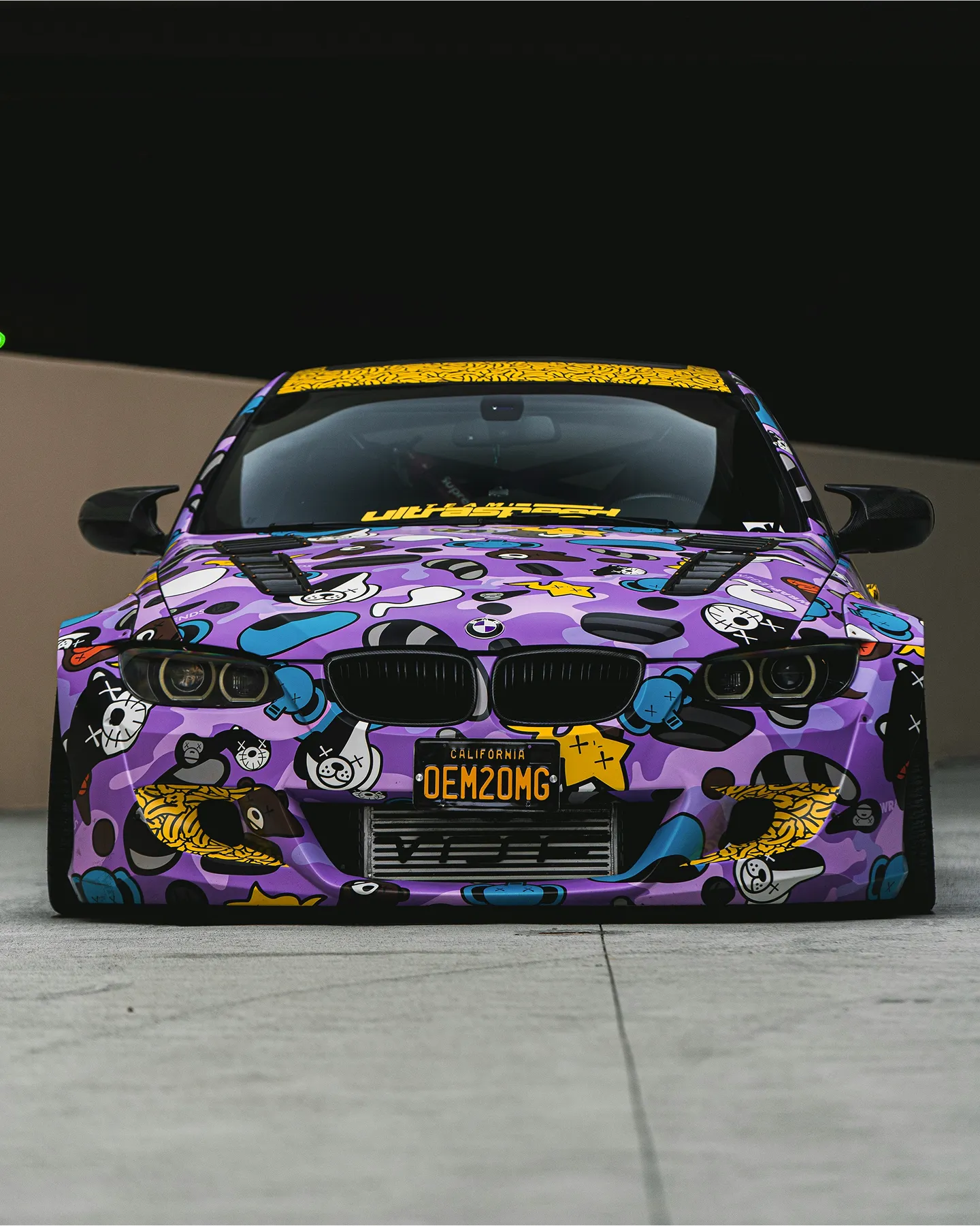 Vibrant purple BMW with cartoon graphics and a dynamic stance, parked against a dark background.