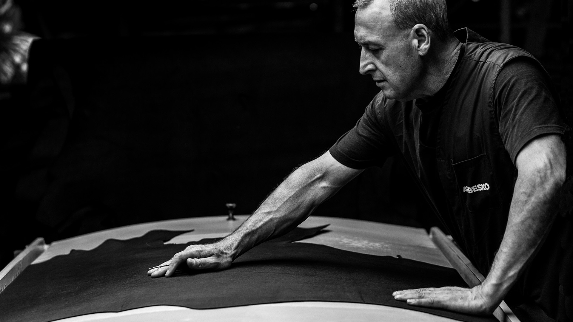 Man som noggrant granskar ett stycke mörkt läder på ett bord.