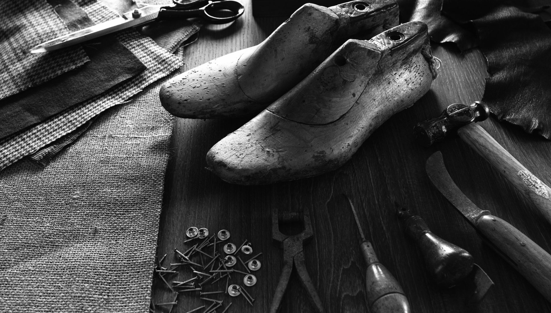 Träsulor, verktyg, tygbitar och små spikar på ett träbord för skotillverkning.