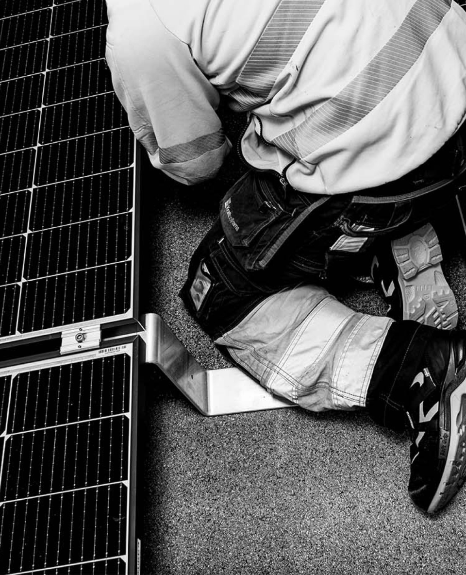Tekniker knäböjer bredvid solpanel och monterar dess fäste på tak.