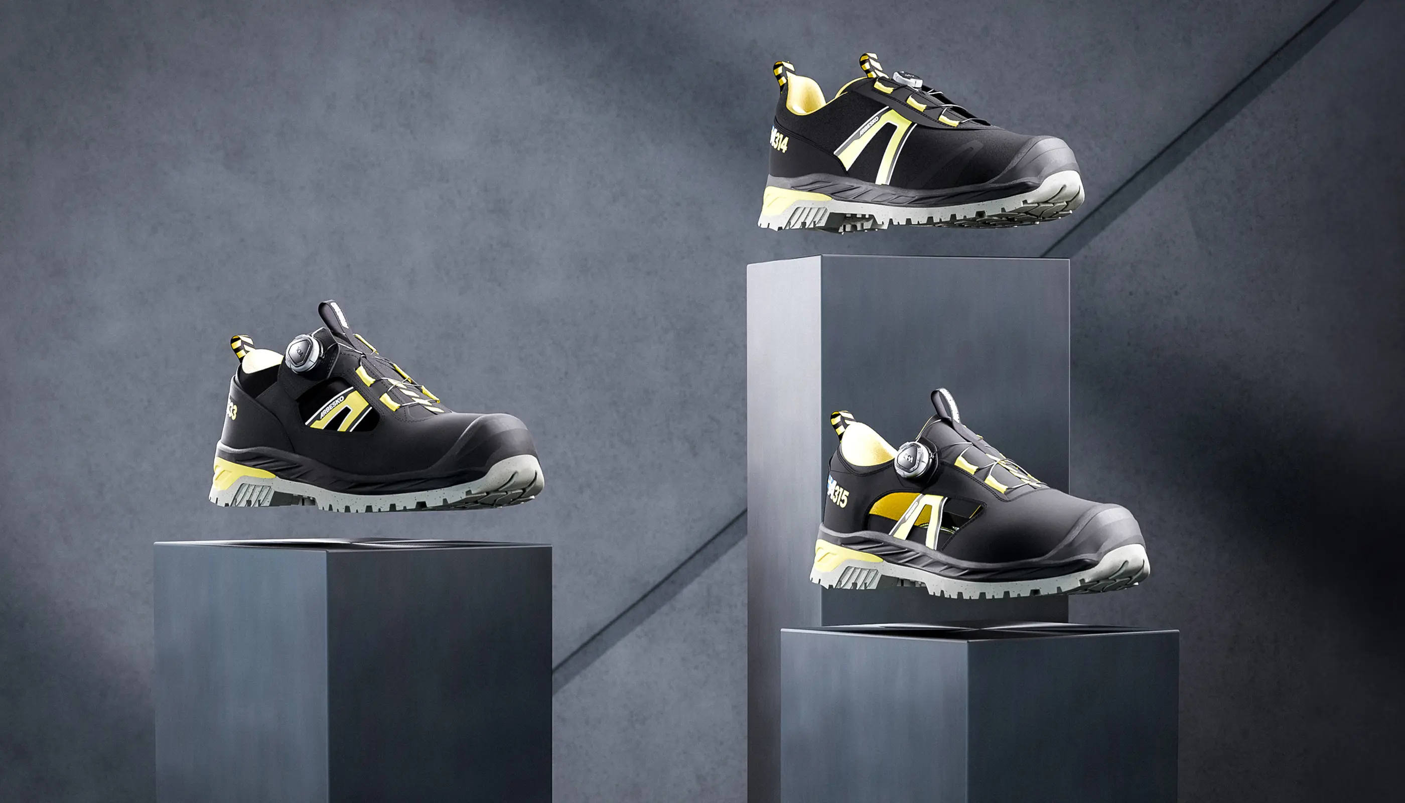 Svarta och gula arbetsskor svävande ovanför mörkgrå piedestaler med en mörk bakgrund.