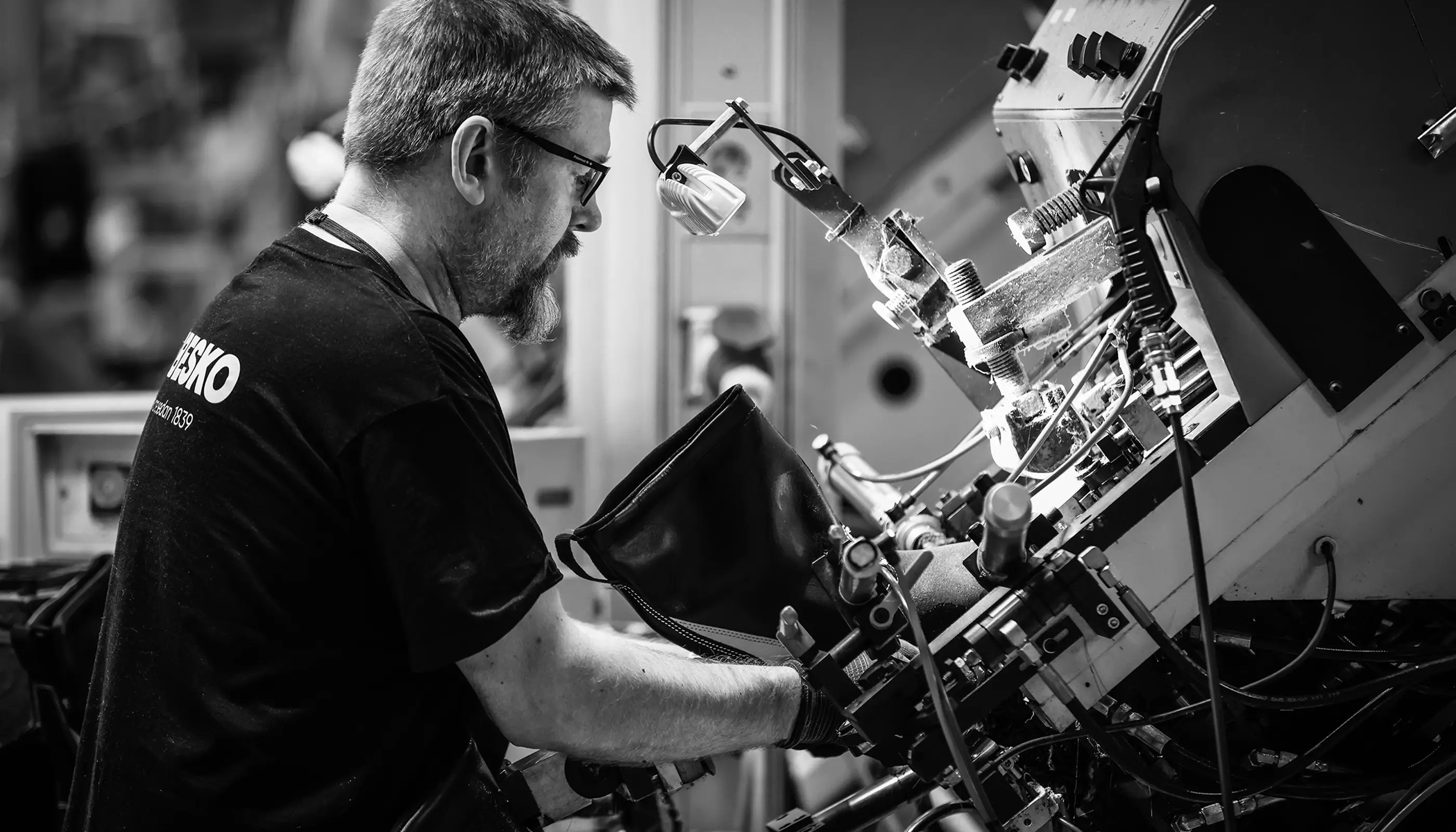 Man med glasögon och skägg arbetar med en avancerad maskin i en industrimiljö.