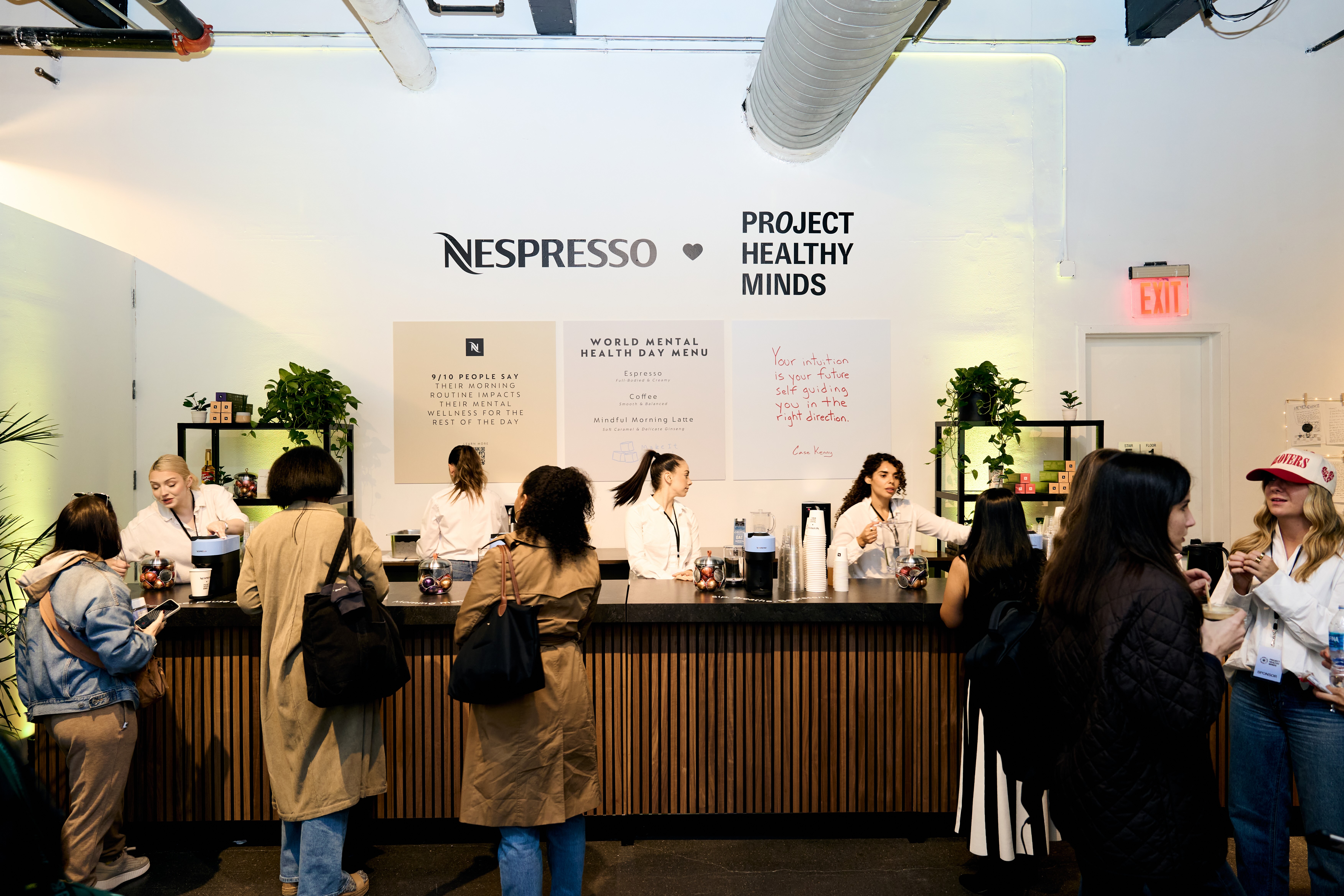 Event coffee bar with Nespresso x Project Healthy Minds branding, guests being served drinks.