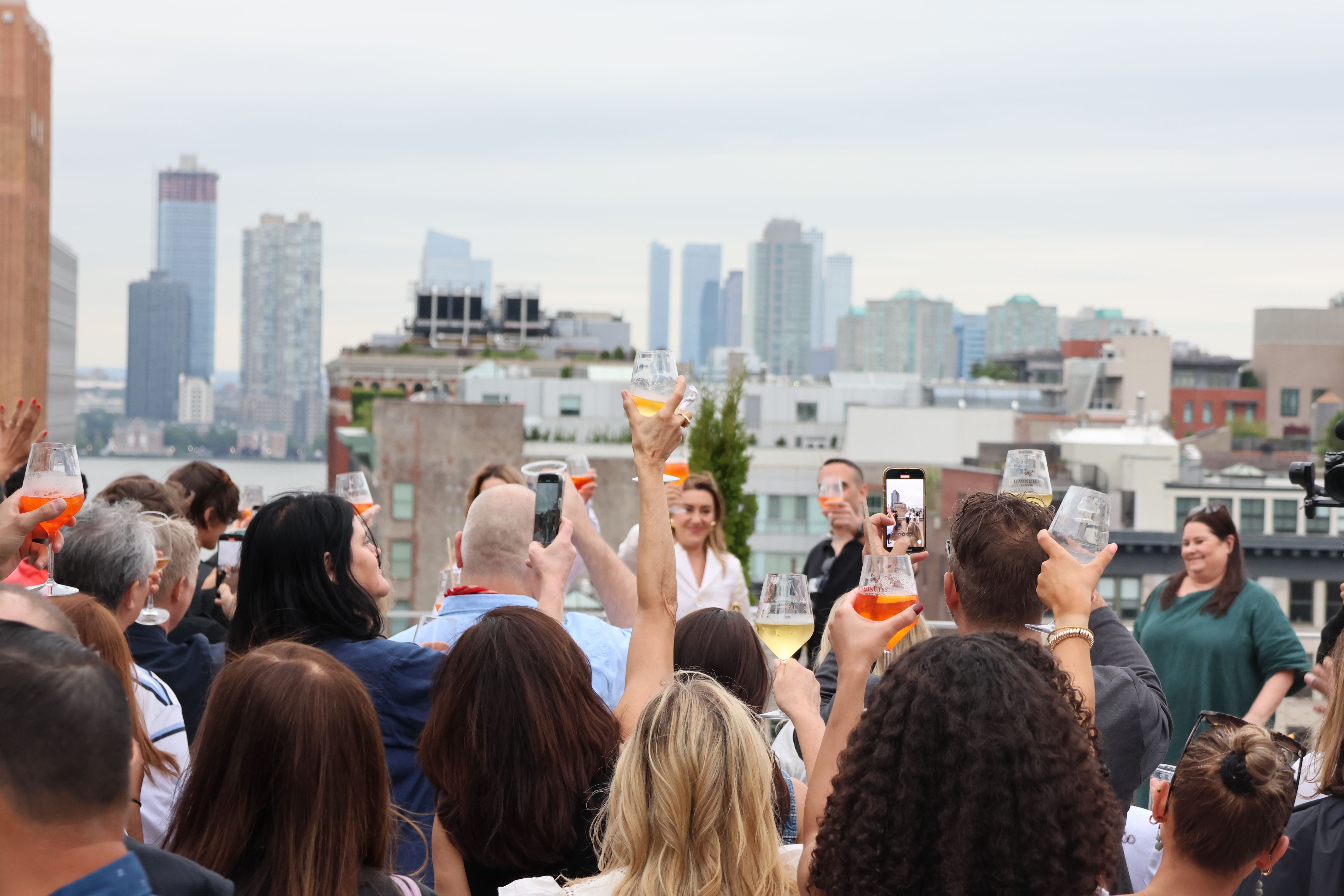 Rooftop gathering with guests raising drinks for a toast against the New York City skyline.