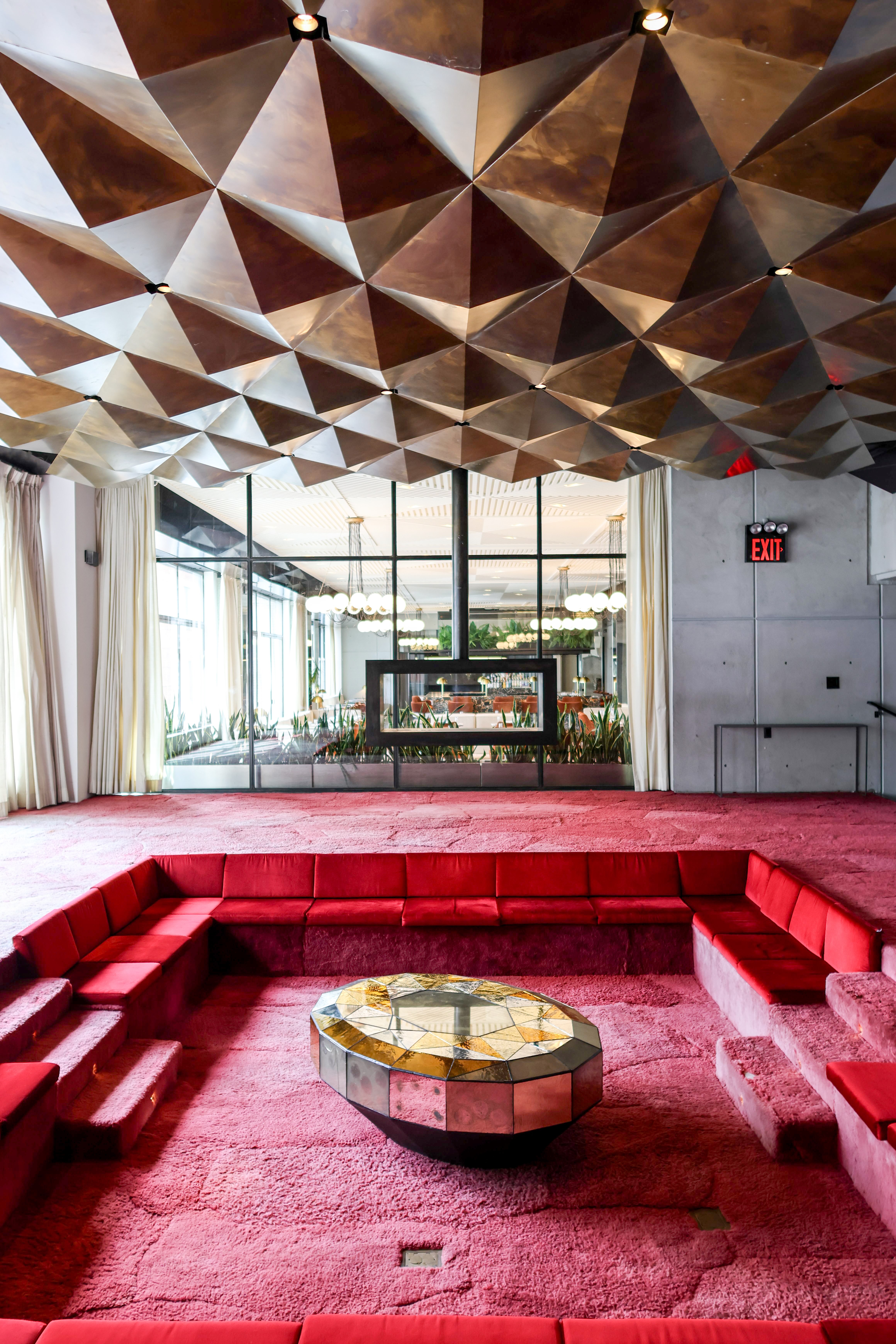 Sunken living room with red seating, geometric mirrored coffee table, and sculptural metallic ceiling.
