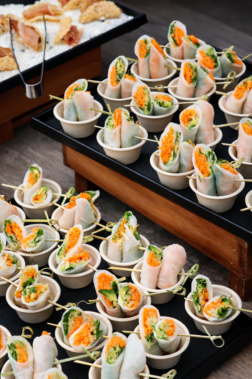 Catered Spring Place spring rolls in small cups arranged on tiered trays.