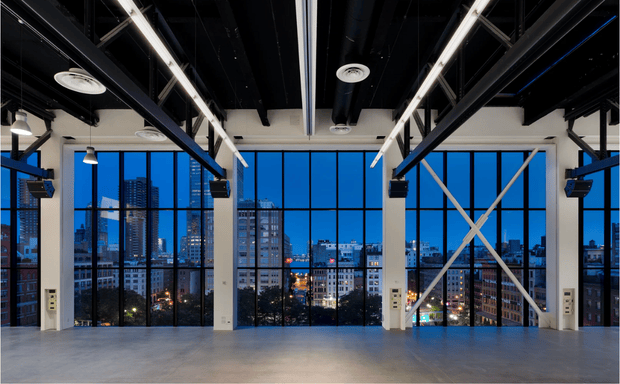 Modern industrial event space with floor-to-ceiling windows overlooking city skyline.