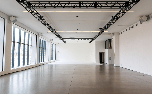 A spacious, empty white room with polished concrete floors, large windows, and black overhead lighting trusses.