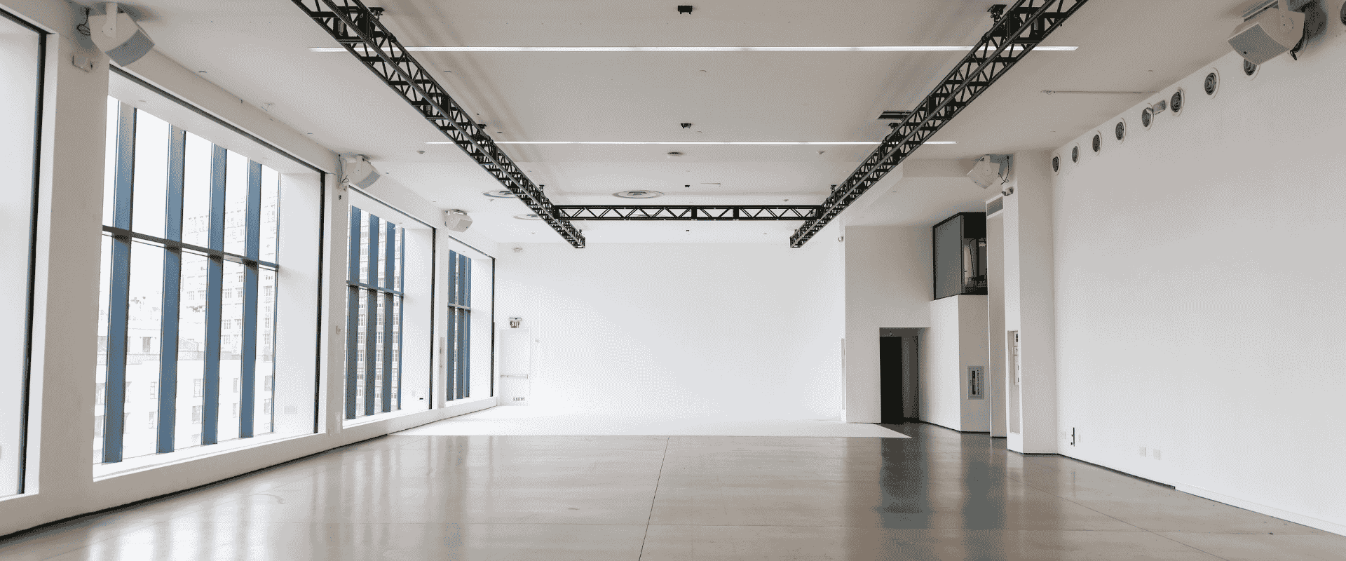 Bright, open event space featuring expansive windows on one side and exposed metal ceiling rigging.