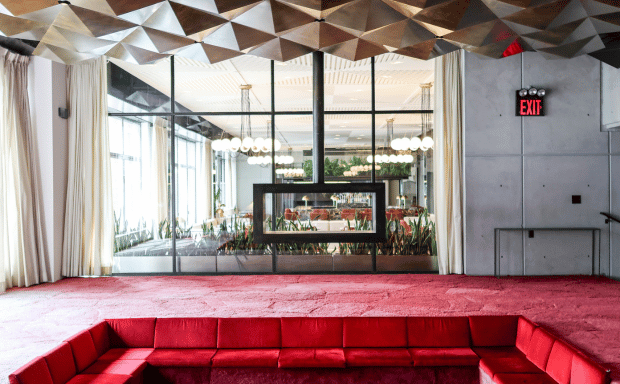 Modern luxury lounge with red velvet couches and geometric ceiling.