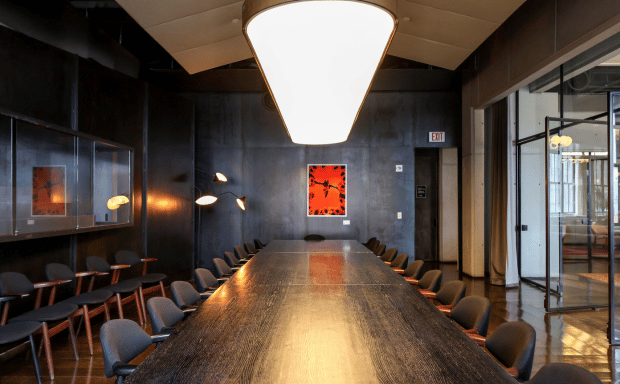 A stylish and moody meeting space with dark-paneled walls, glass partitions on the right, and a pop of vibrant color from a red framed artwork on the back wall.