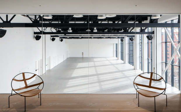 A spacious, empty white event hall viewed from an elevated wooden loft featuring two round accent chairs.