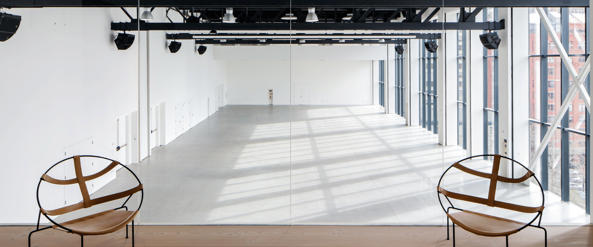 Two modern circular chairs overlook a vast, open venue below with large windows and black steel ceiling beams.