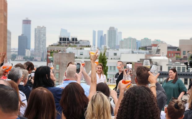 Guests raising drinks toward the Manhattan skyline on the Spring Studios Tribeca rooftop during a corporate summer event