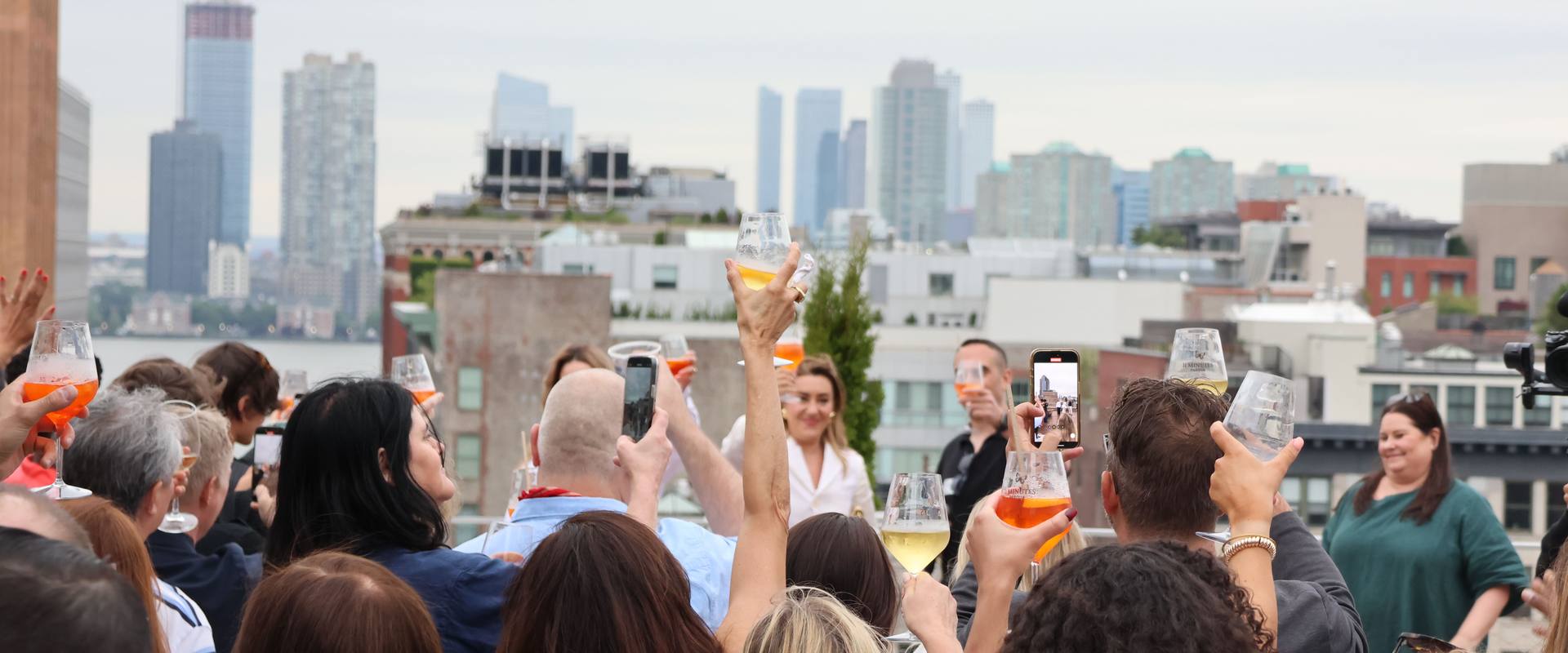 Corporate summer event on the Spring Studios Tribeca rooftop, guests toasting with the New York City skyline in the background