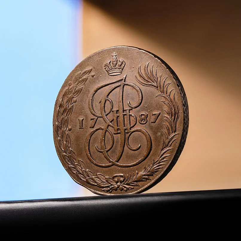 Oude koperen munt uit 1787 met een gekroond monogram en een krans van bladeren aan beide zijden. 