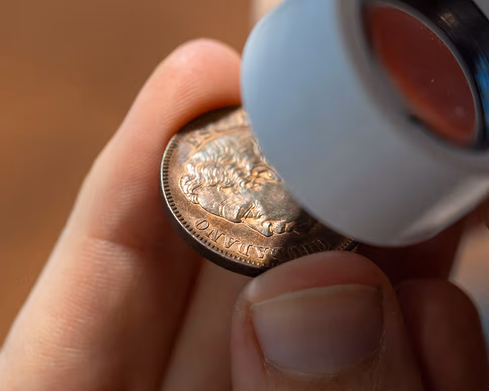 Hand die een munt van dichtbij onderzoekt met een vergrootglas.