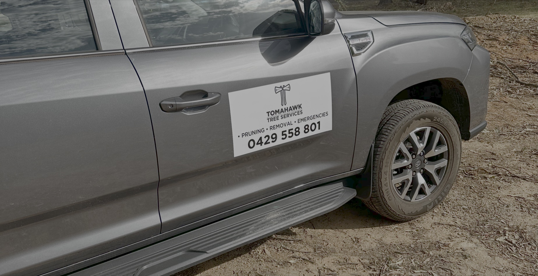 Silver vehicle door with a Tomahawk Tree Services sign showing contact for pruning and removal services.